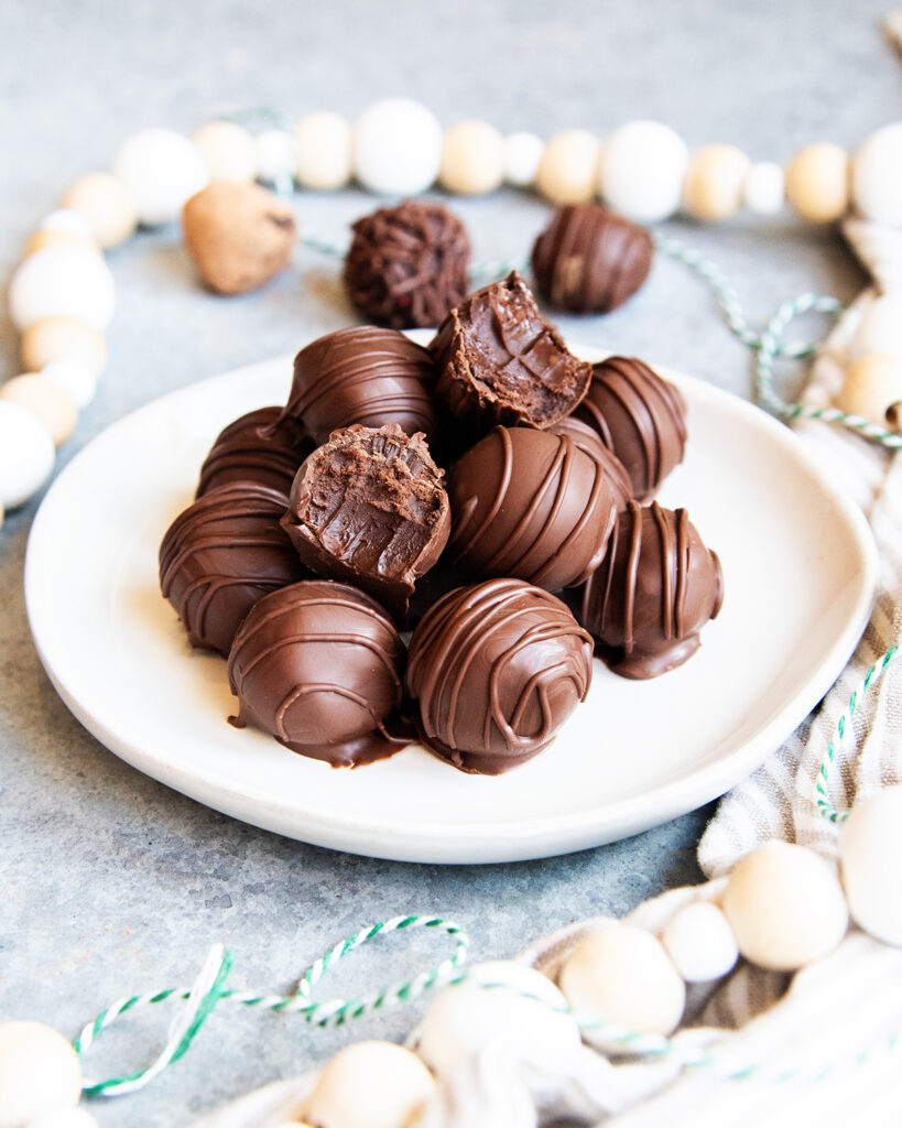 A plate of a pile of chocolate truffles, with two that have a bite out of them, showing the soft truffle center.