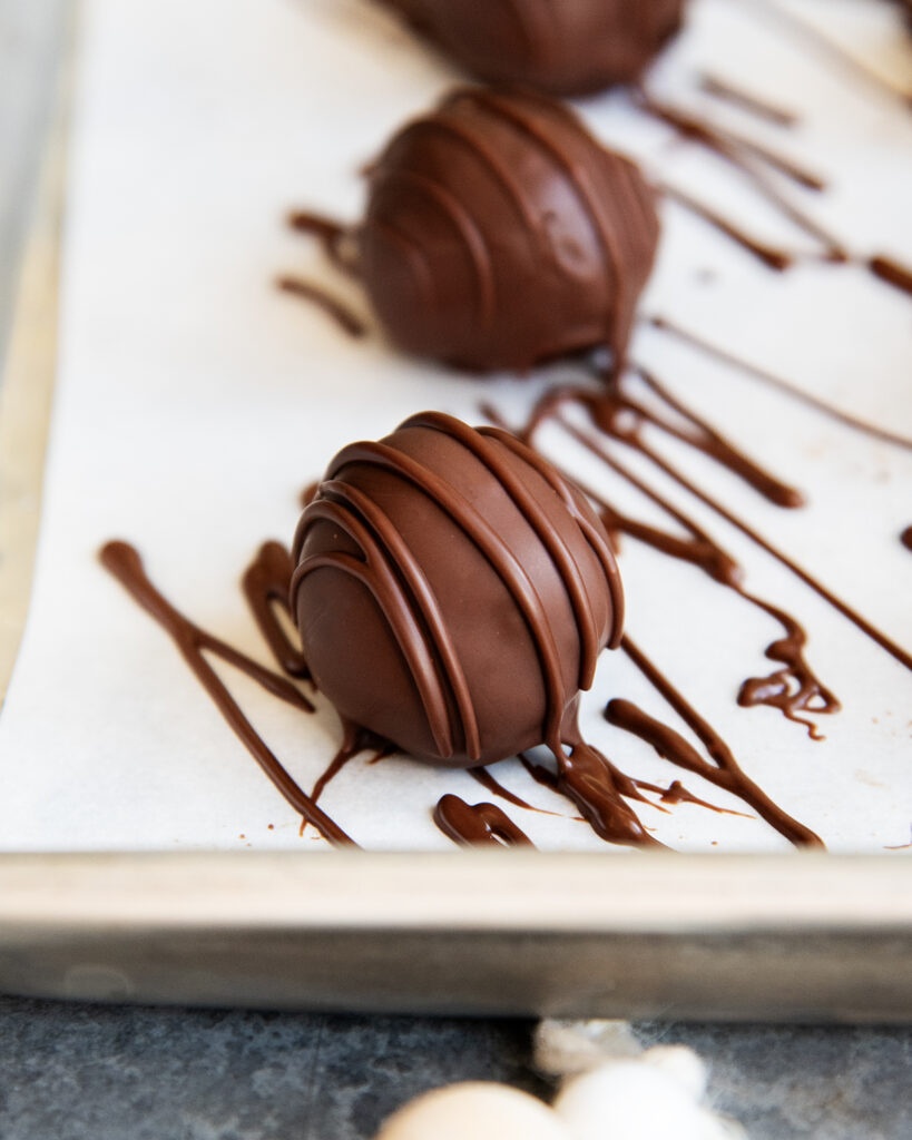 A close up of a chocolate mint truffle drizzled with extra chocolate on a cookie sheet.