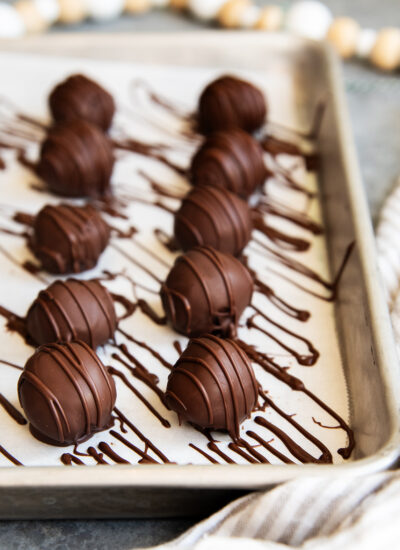 Two rows of chocolate mint truffles drizzled with extra chocolate on a cookie sheet.