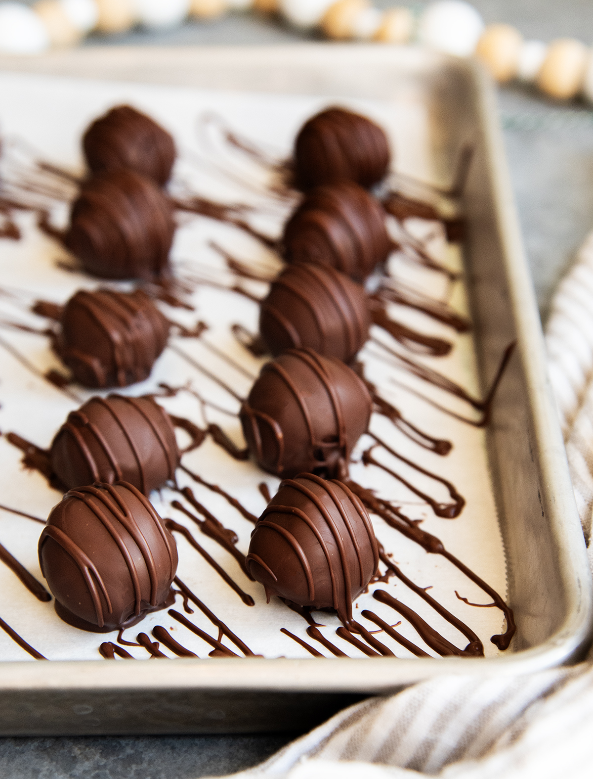 Two rows of chocolate mint truffles drizzled with extra chocolate on a cookie sheet.