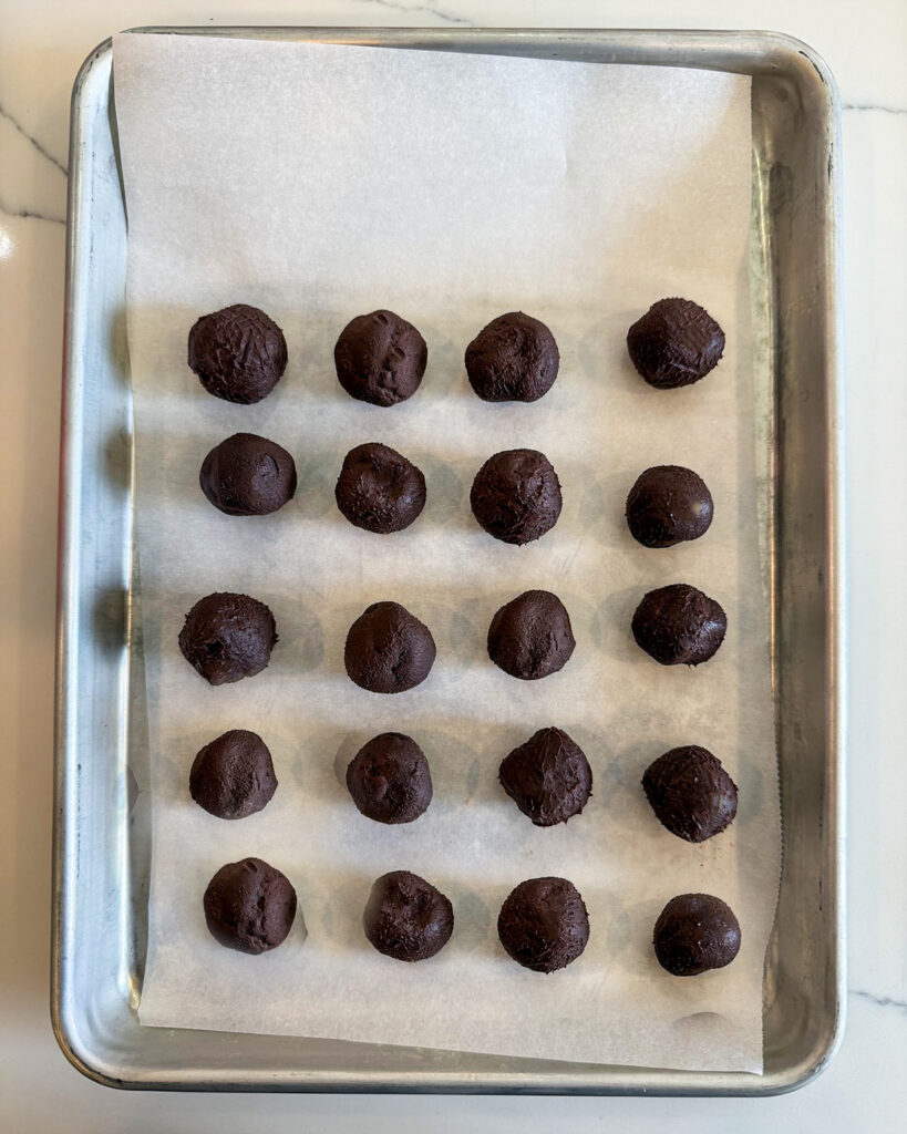 Rolled up chocolate truffles on a parchment paper lined cookie sheet.