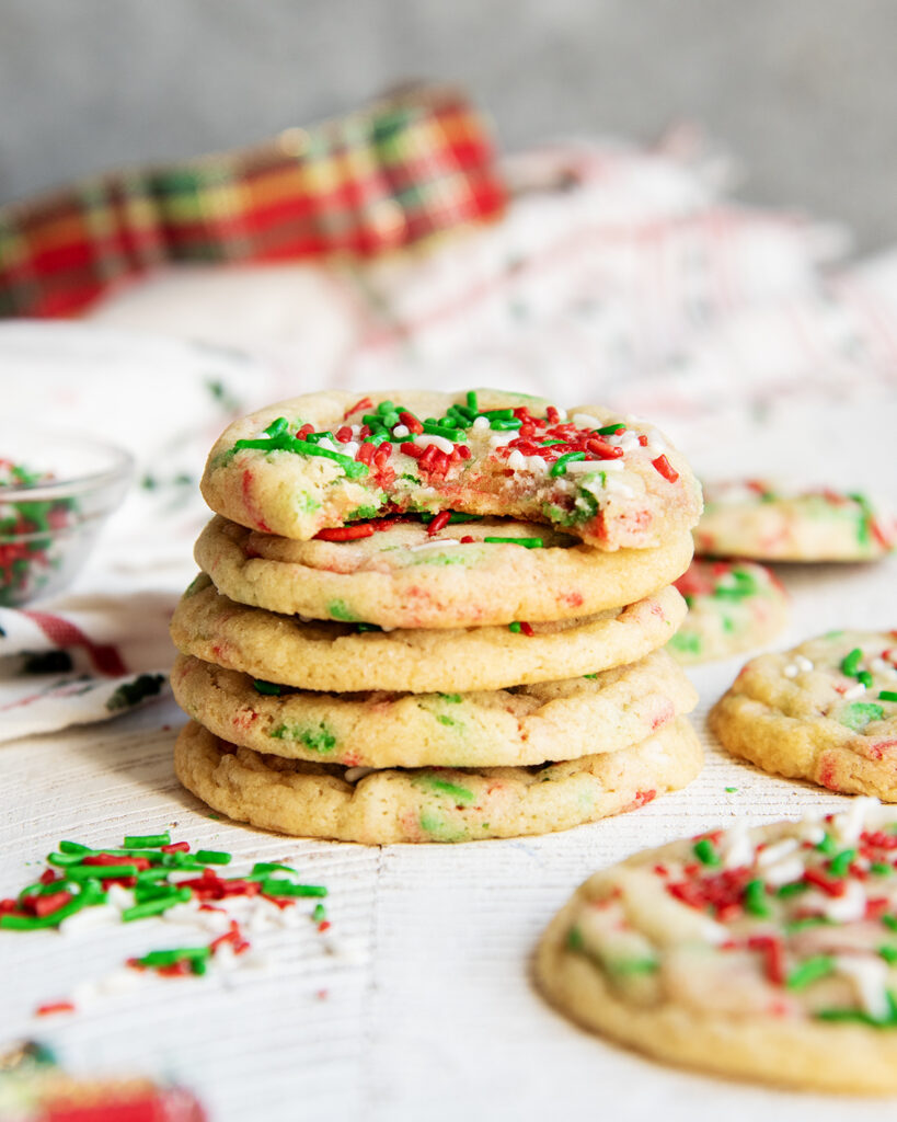 A stack of 5 Christmas Funfetti cookies with red, white, and green sprinkles. The top cookie has a bite out of it.