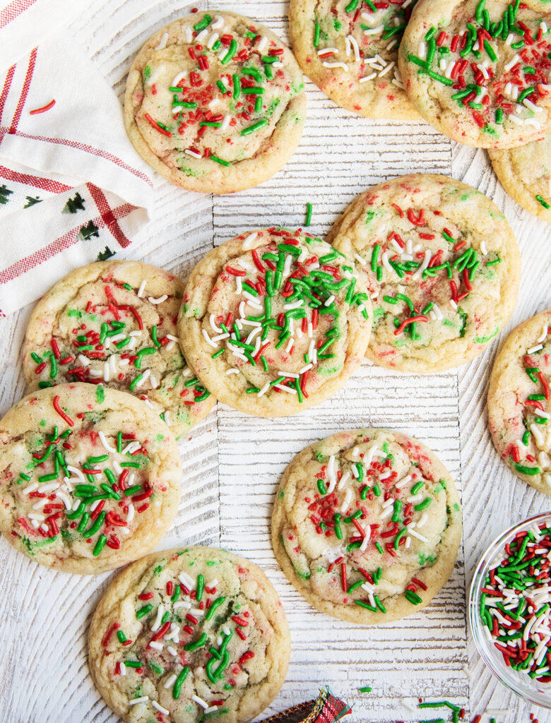 Christmas Sprinkle cookies on a white table, with a Christmas towel next to them.