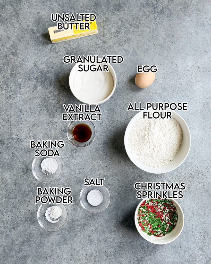 Bowls of the ingredients needed to make Christmas Sprinkle Sugar Cookies, including granulated sugar, flour, vanilla, and Christmas Sprinkles. 