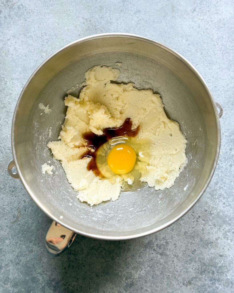 A bowl of creamed butter, topped with an egg, and vanilla extract. 