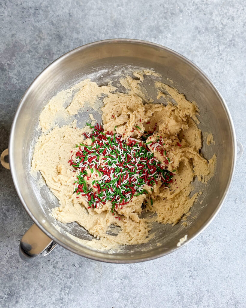 A bowl of sugar cookie dough topped with red, white and green sprinkles.