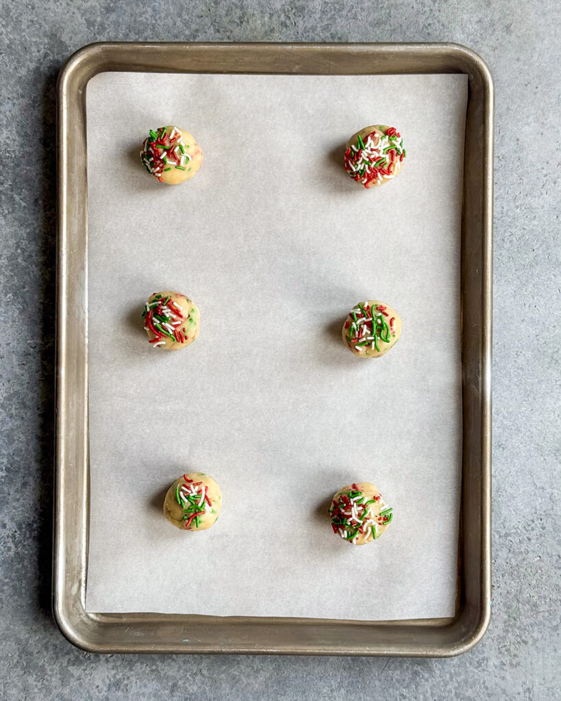 Six Christmas Sprinkle Cookie Dough balls on a cookie tray.