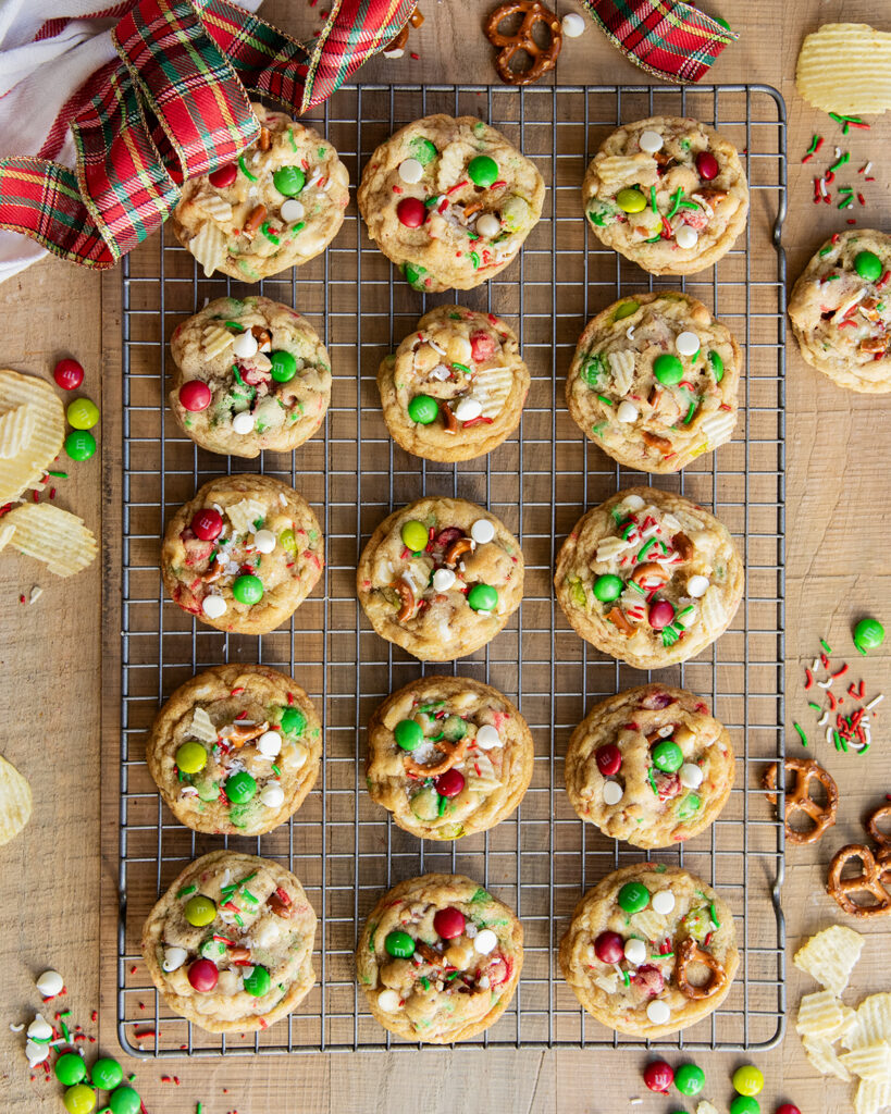 Christmas Kitchen Sink Cookies on a wire cooling rack topped with Christmas m&ms, white chocolate chips, pretzels, and ruffles chips.