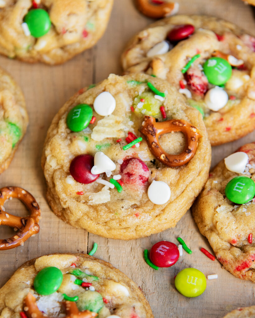 A stack of Kitchen Sink Cookies, topped with white chocolate chips, Christmas m&ms, and pretzels. 