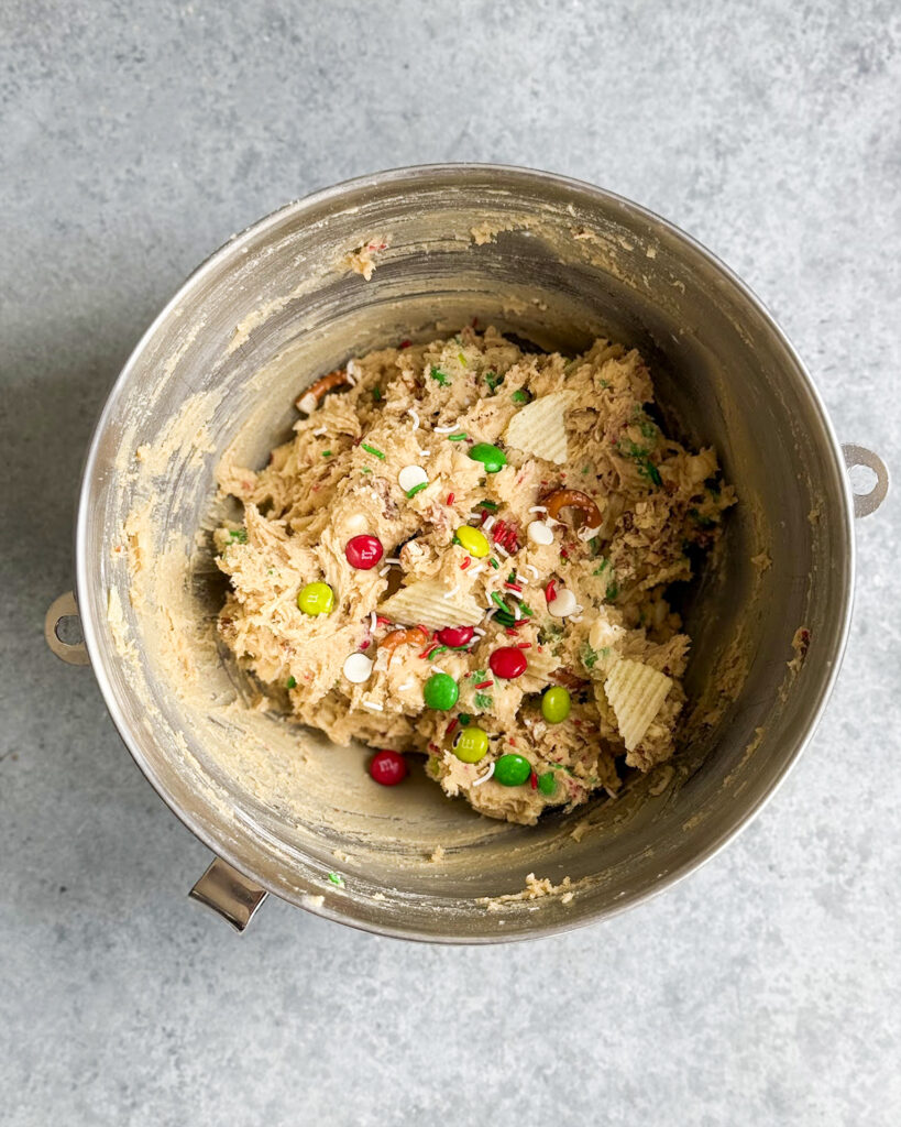 A bowl of cookie dough topped with m&ms, sprinkles, pretzels, and potato chips. 