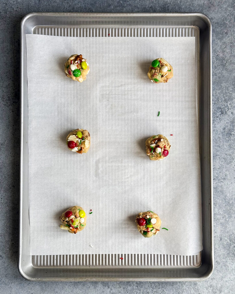 Six balls of cookie dough topped with m&ms and white chocolate chips. 