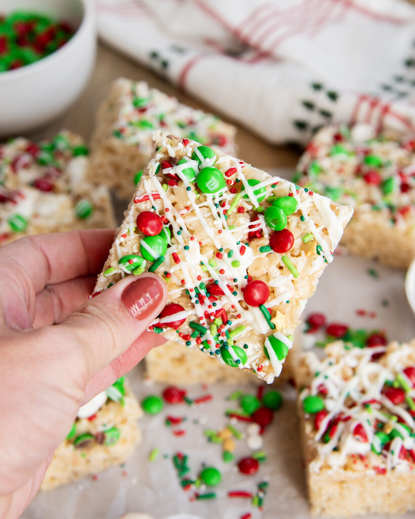 A hand holding a Christmas Rice Krispie Treat topped with Christmas m&ms and sprinkles.