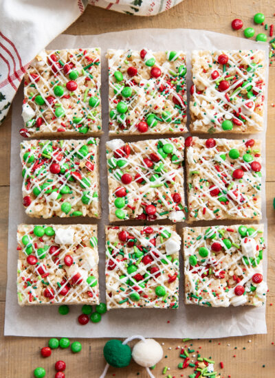 Rows of rice krispie treats topped with white chocolate, and red and green sprinkles, and m&ms.