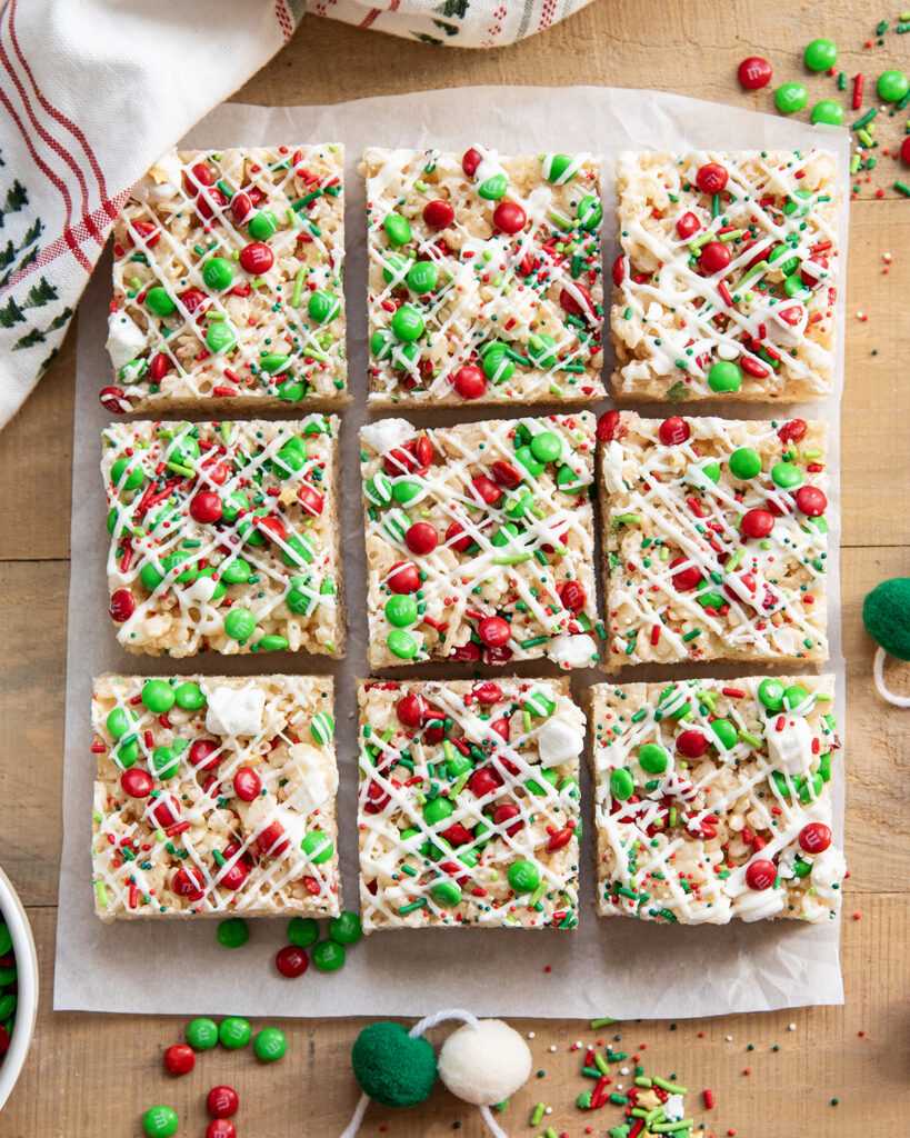 Rows of rice krispie treats topped with white chocolate, and red and green sprinkles, and m&ms.