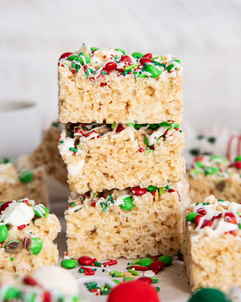 A stack of three rice krispie treats each topped with festive Christmas m&ms and sprinkles.