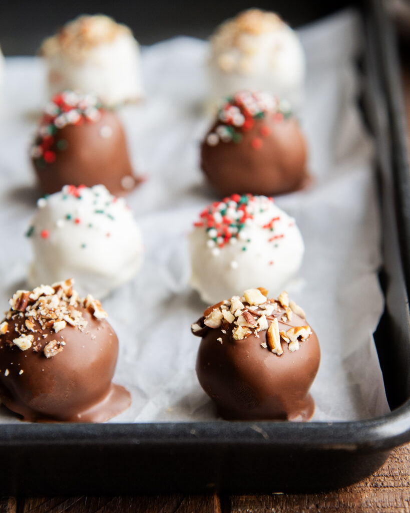 Rows of Pecan Pie Balls on a cookie sheet, coated in chocolate and white chocolate.