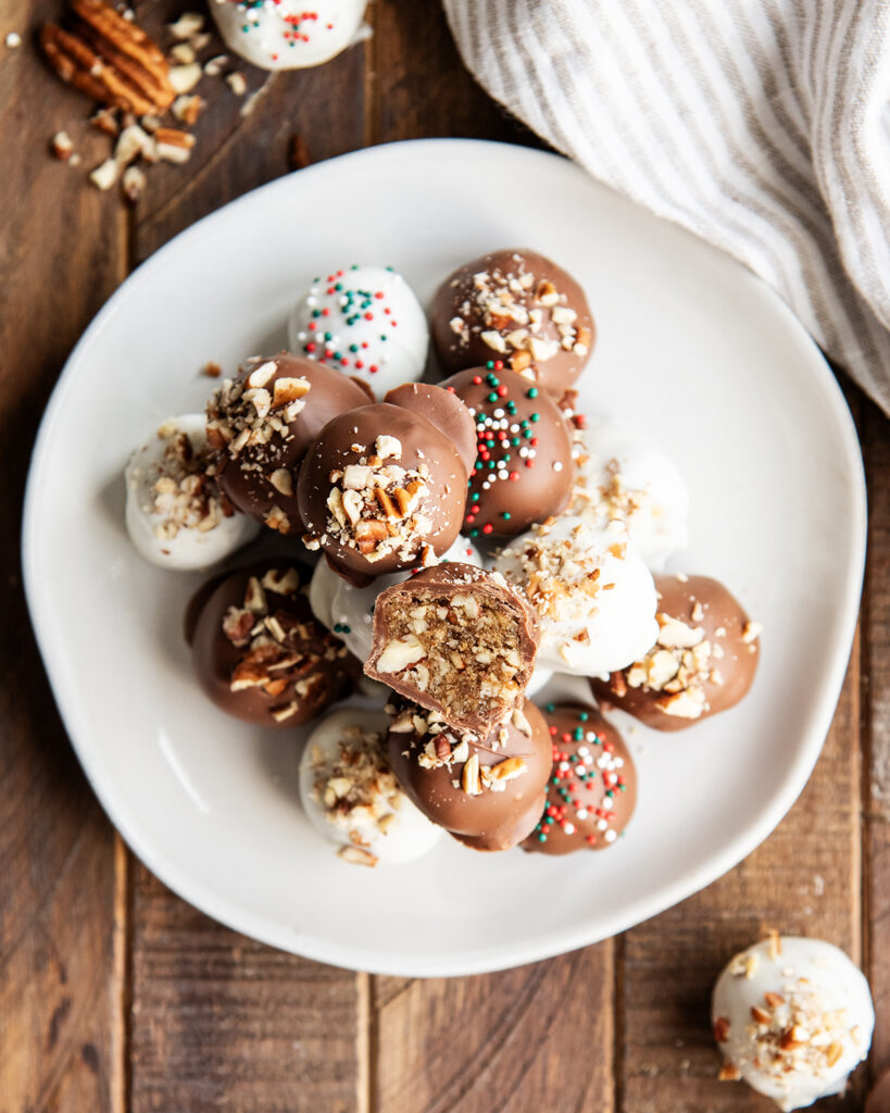 A pile of pecan pie balls on a plate, one is cut in half showing the pecan pie filling.