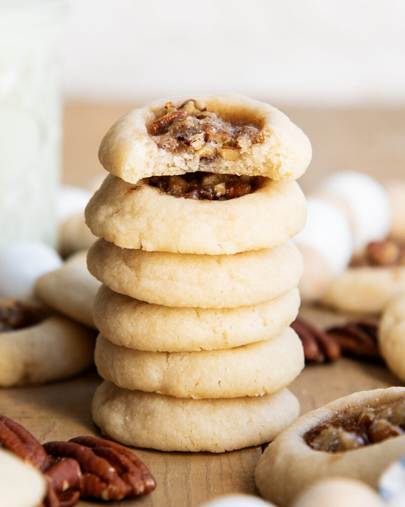 A stack of pecan pie thumbprint cookies, and the top cookie has a bite out of it.