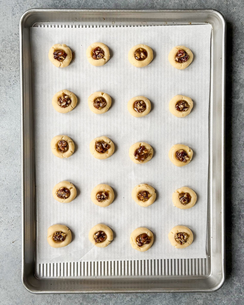 An above view of a pan of unbaked pecan pie thumbprint cookies.