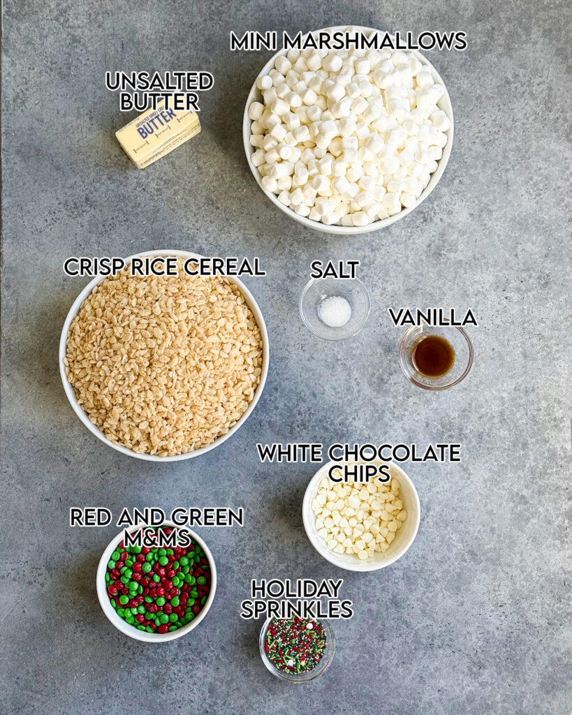 Small bowls of the ingredients needed to make Christmas Rice Krispie Treats, including mini marshmallows, crisp rice cereal, m&ms, and white chocolate chips. 