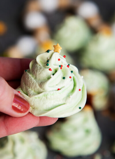 A hand holding a green Christmas tree decorated meringue cookie topped with a golden star sprinkle.