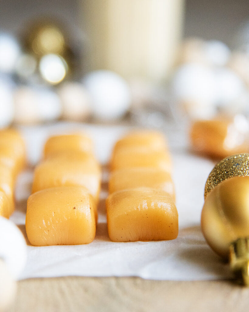 Rows of eggnog caramels next to ornaments on a tab le. 