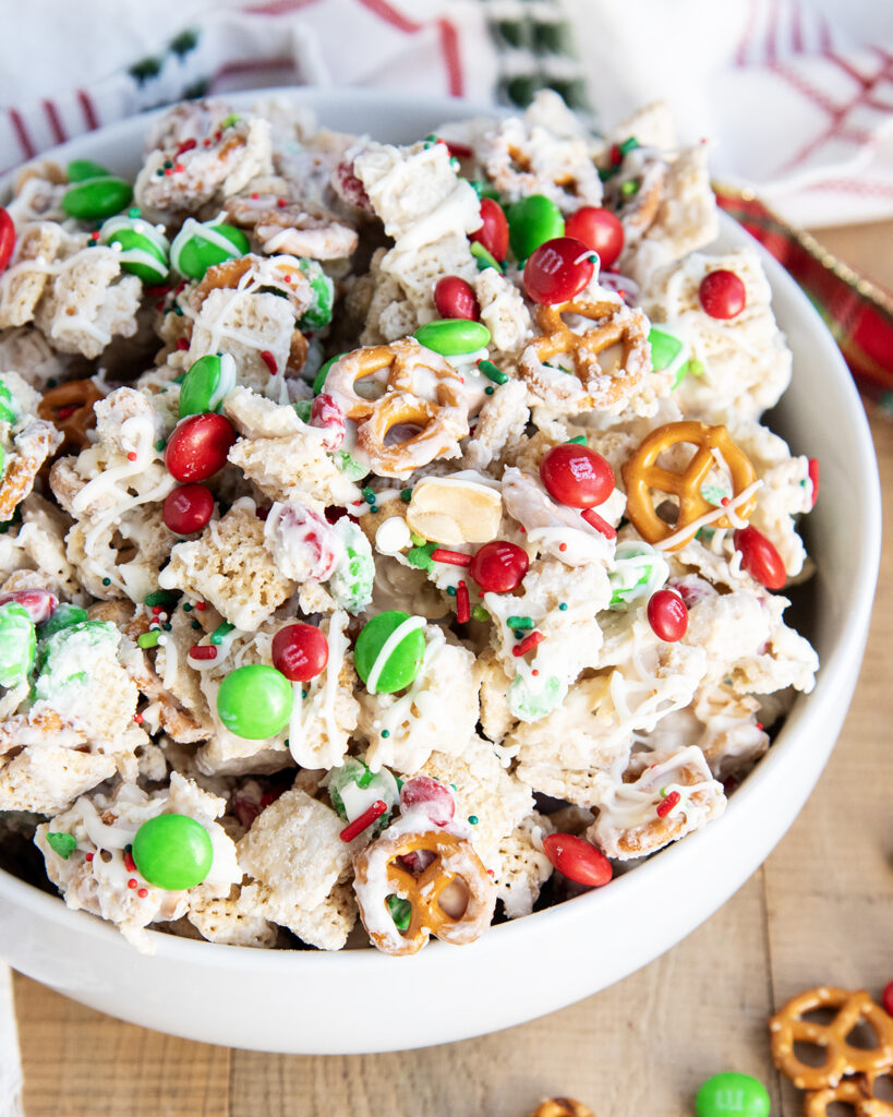 A close up of a bowl of white trash chex mix with mini pretzels and m&ms.