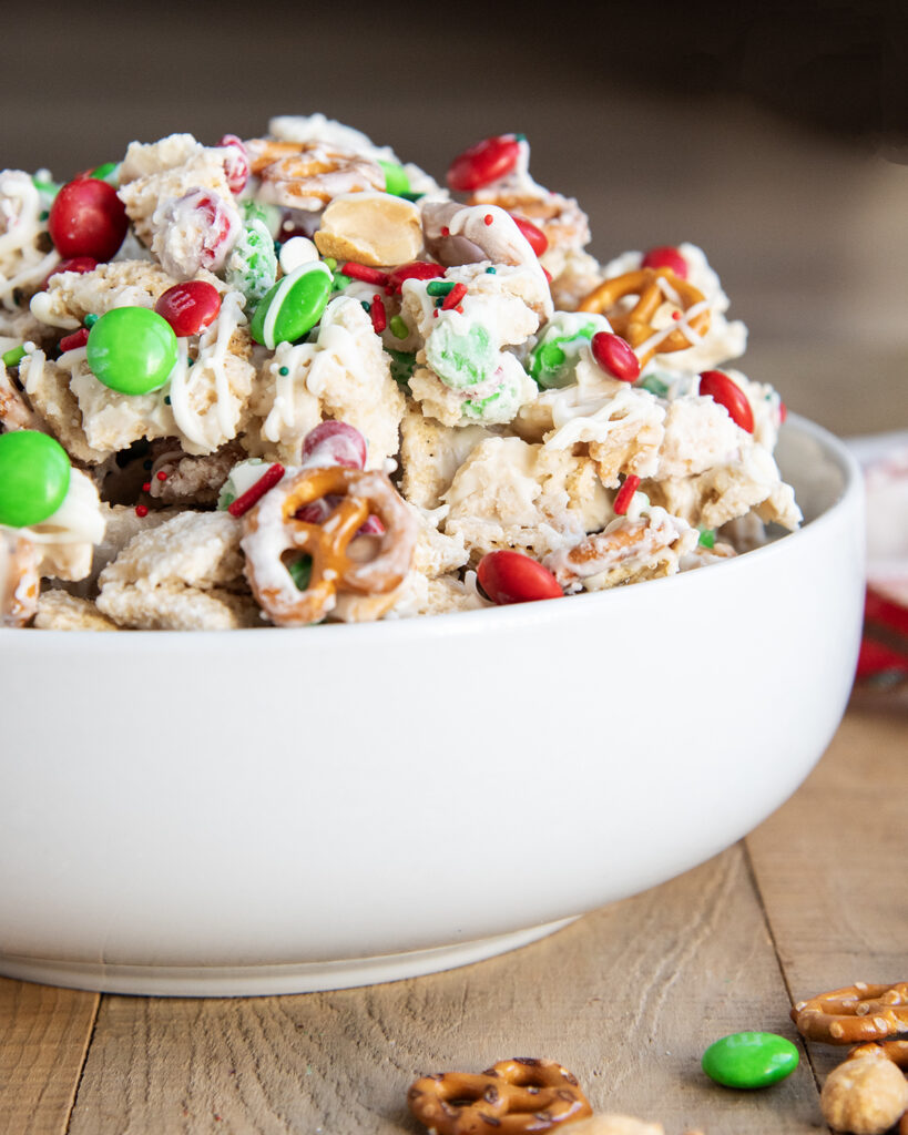 A close up of a bowl of white trash chex mix with mini pretzels and m&ms.