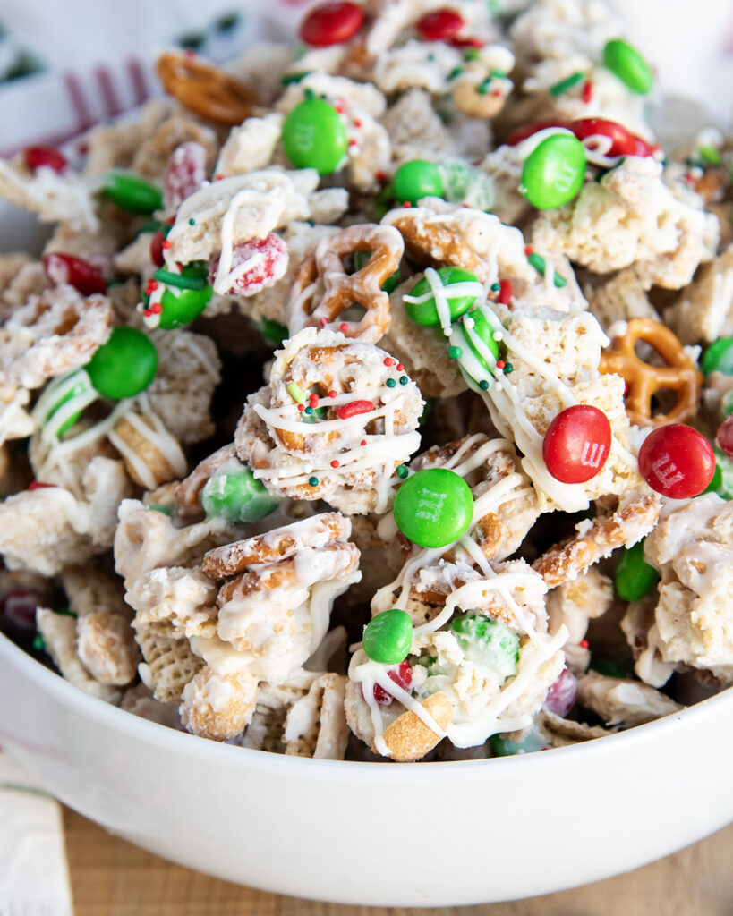 A close up of a bowl of white trash chex mix with mini pretzels and m&ms.