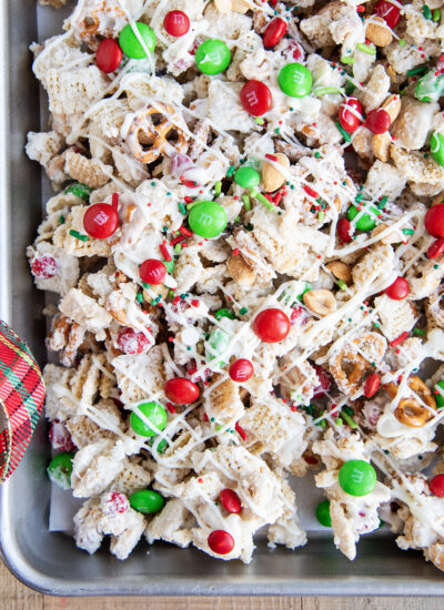 An above view of a pan of white chocolate chex mix topped with red and green m&ms.