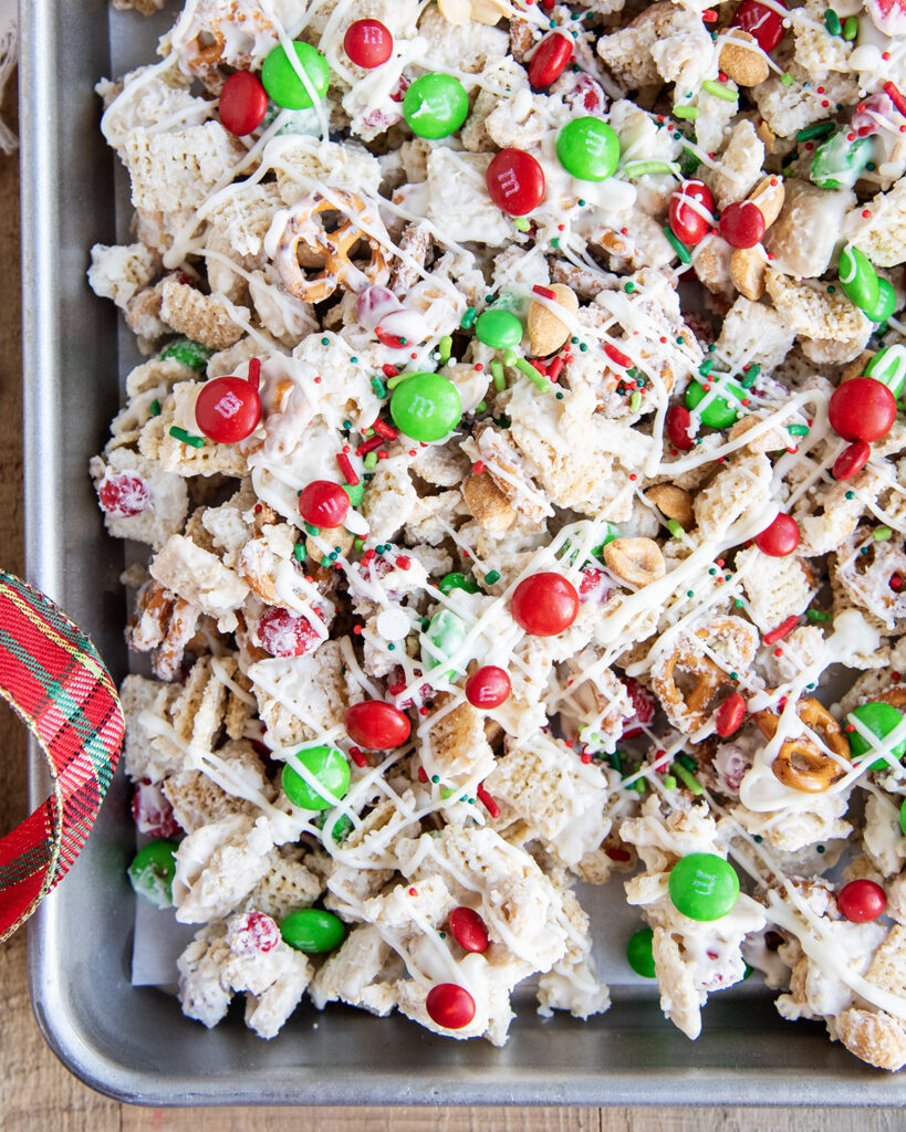 An above view of a pan of white chocolate chex mix topped with red and green m&ms. 