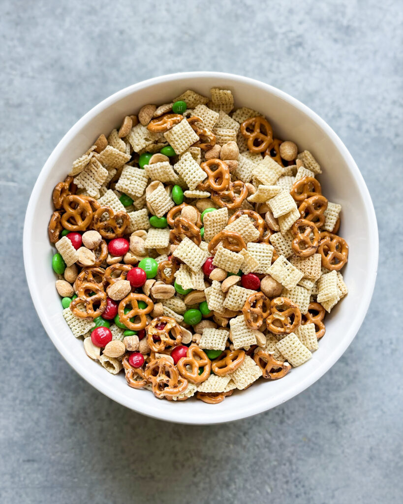 A bowl of chex mixed with mini pretzels, peanuts, and m&ms. 