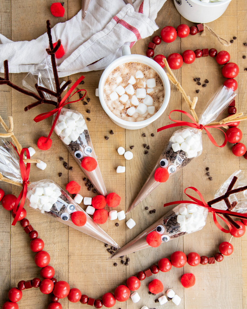 An above view of a cup of hot cocoa with marshmallows, and a hot chocolate bag full of cocoa mix, mini marshmallows, and chocolate chips.