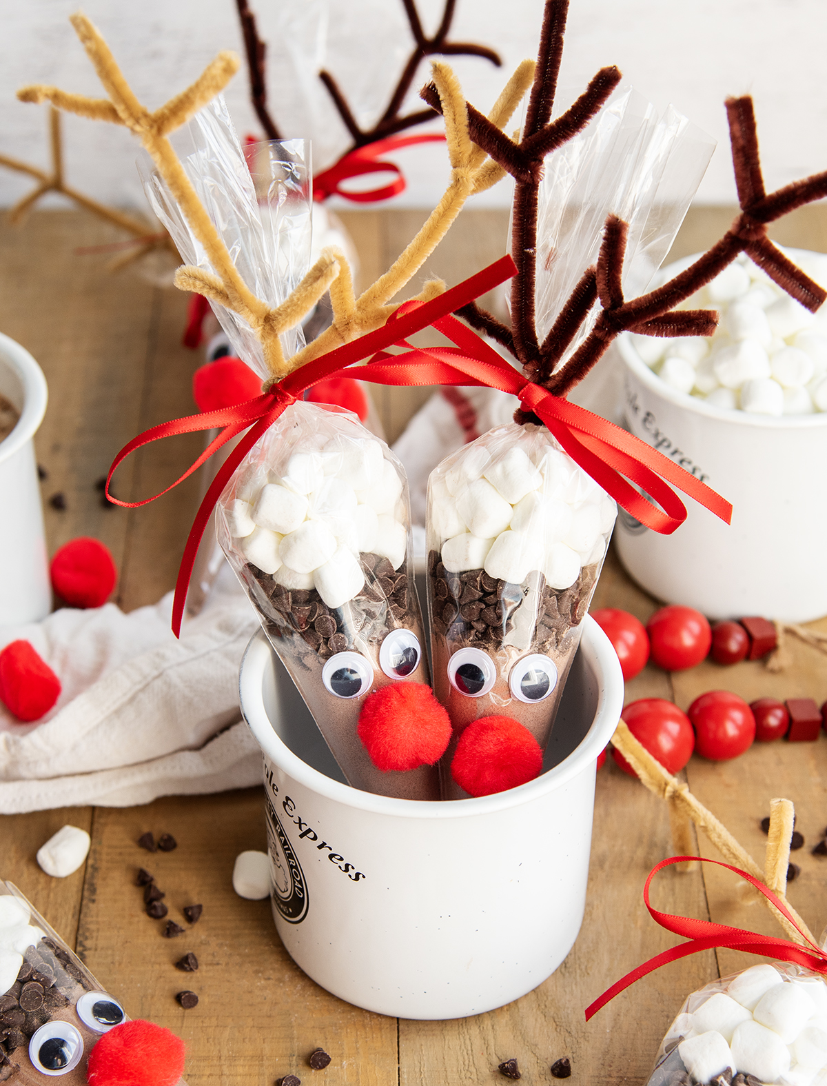 Two Reindeer Hot Chocolate packs in reindeer decorated bags sitting in a porcelain mug.