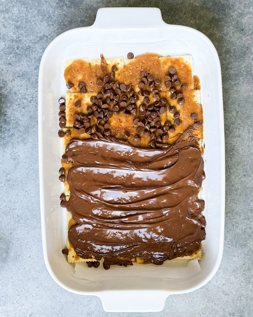 Salting toffee topped with chocolate chips, and melted chocolate that is spread too.