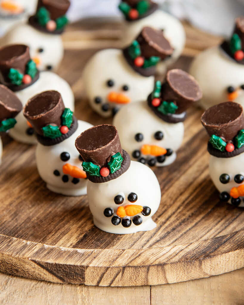 Cookie Dough balls dipped in white chocolate and decorated to look like a snowman with candy eyes, a sprinkle nose and a rolo hat.