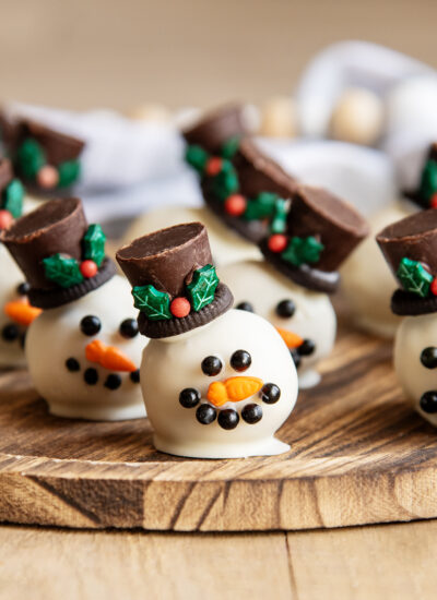 Cookie Dough balls dipped in white chocolate and decorated to look like a snowman with candy eyes, a sprinkle nose and a rolo hat.