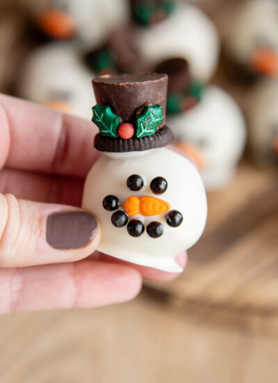 A hand holding a cookie dough ball decorated to look like a snowman head.