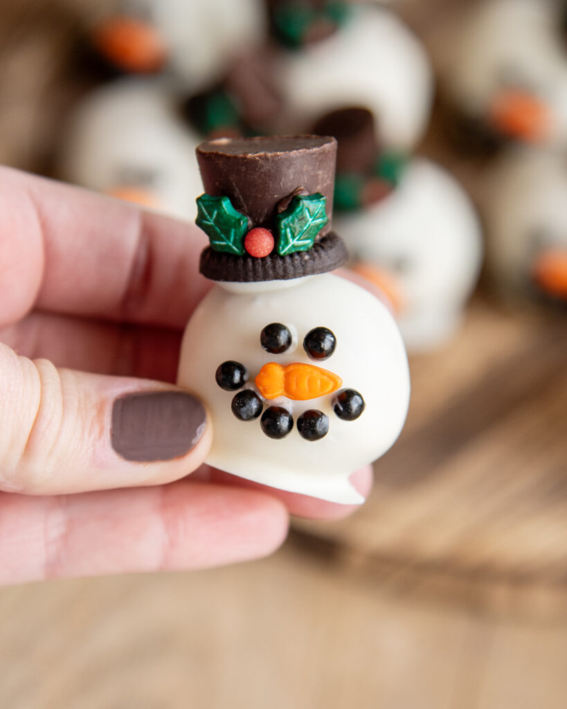 A hand holding a cookie dough ball decorated to look like a snowman head.