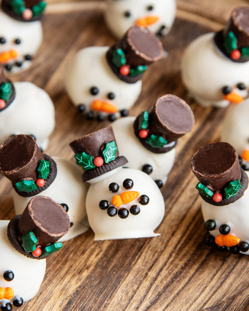 Cookie dough balls dipped in white chocolate and decorated to look like snowmen on a wooden board.