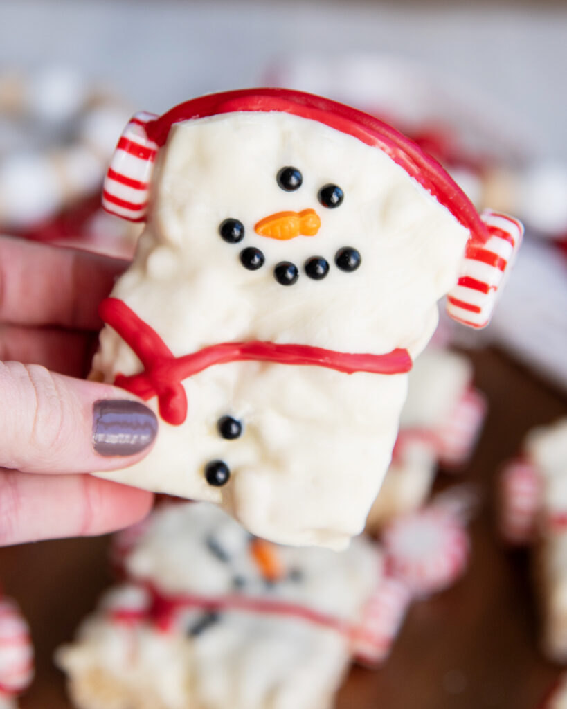 A hand holding a snowman decorated rice krispie treat.