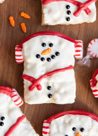 A square rice krispie treat decorated with candy and sprinkles to look like a snowman.