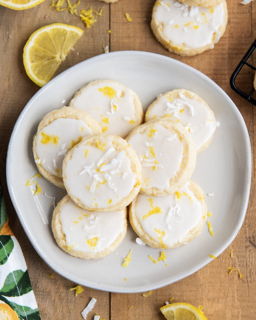 An above view of a pile of glazed coconut lemon shortbread cookies on a plate.