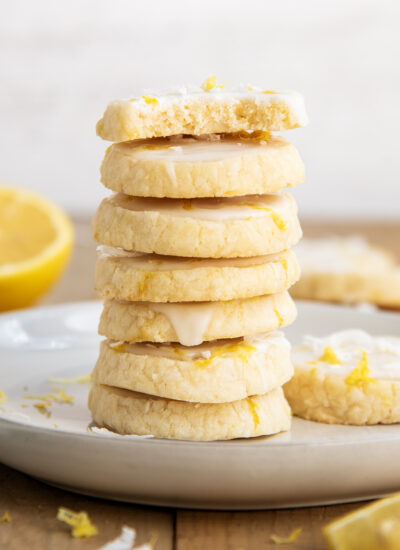 A stack of coconut lemon shortbread cookies on a white plate, the top cookie has a bite out of it.