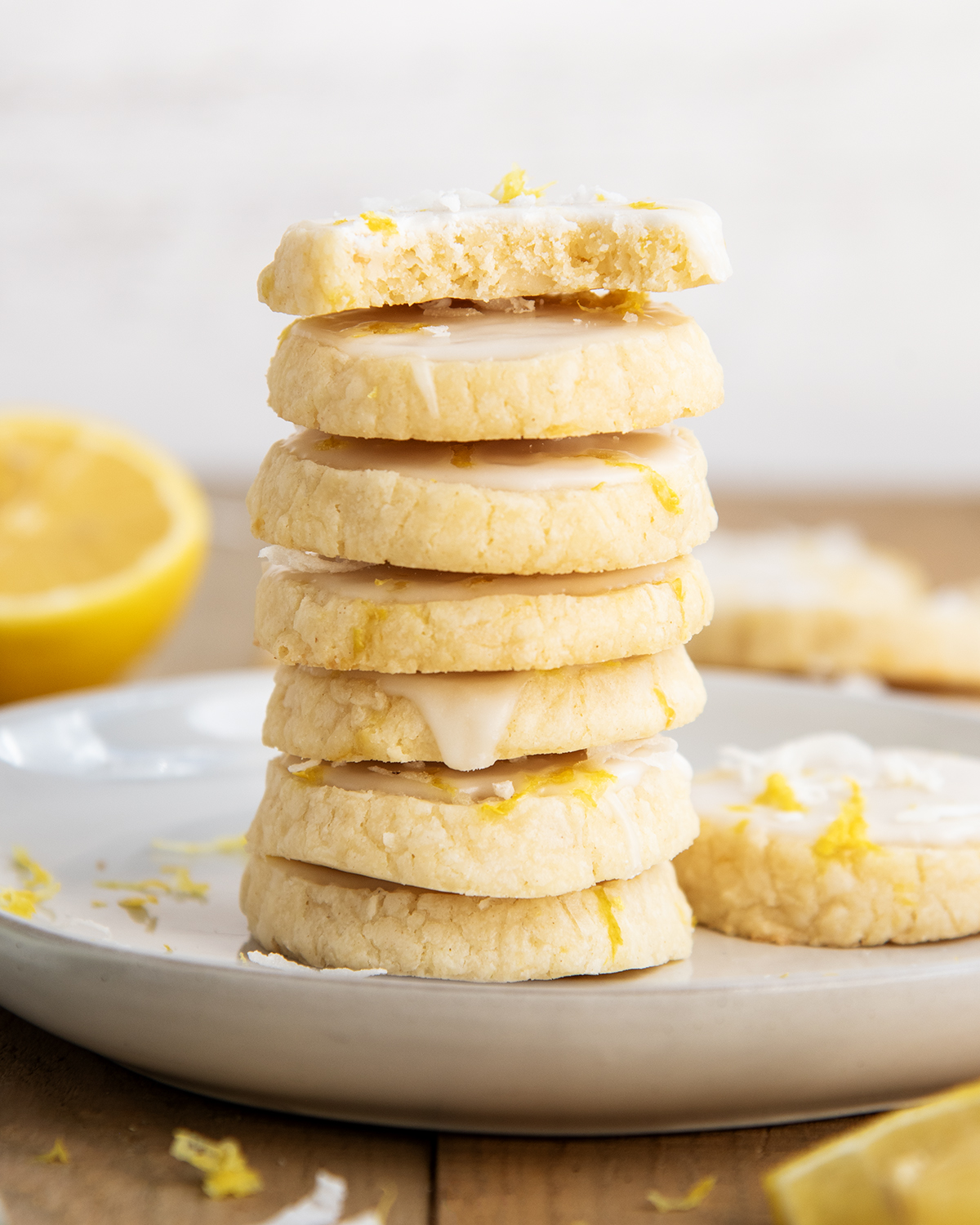 A stack of coconut lemon shortbread cookies on a white plate, the top cookie has a bite out of it.