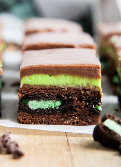 A Mint Oreo Brownie with a mint oreo in the middle of a brownie topped with a green frosting and chocolate fudge.