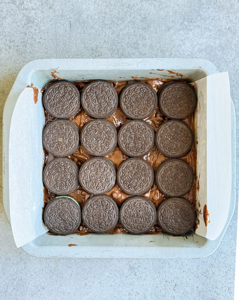 Brownie batter topped with a layer of oreos in a square pan.