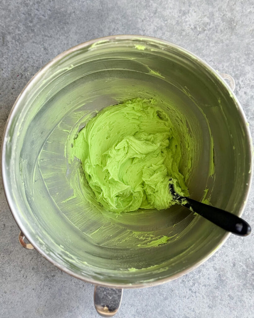 A green frosting in a metal bowl.