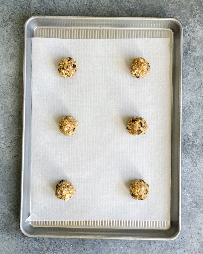 Six oatmeal toffee cookie dough balls on a cookie sheet.