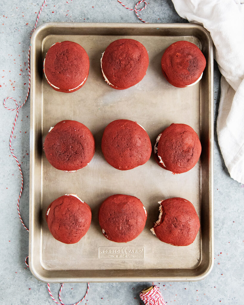 An above view of red velvet cookie sandwiches on a metal cookie sheet.